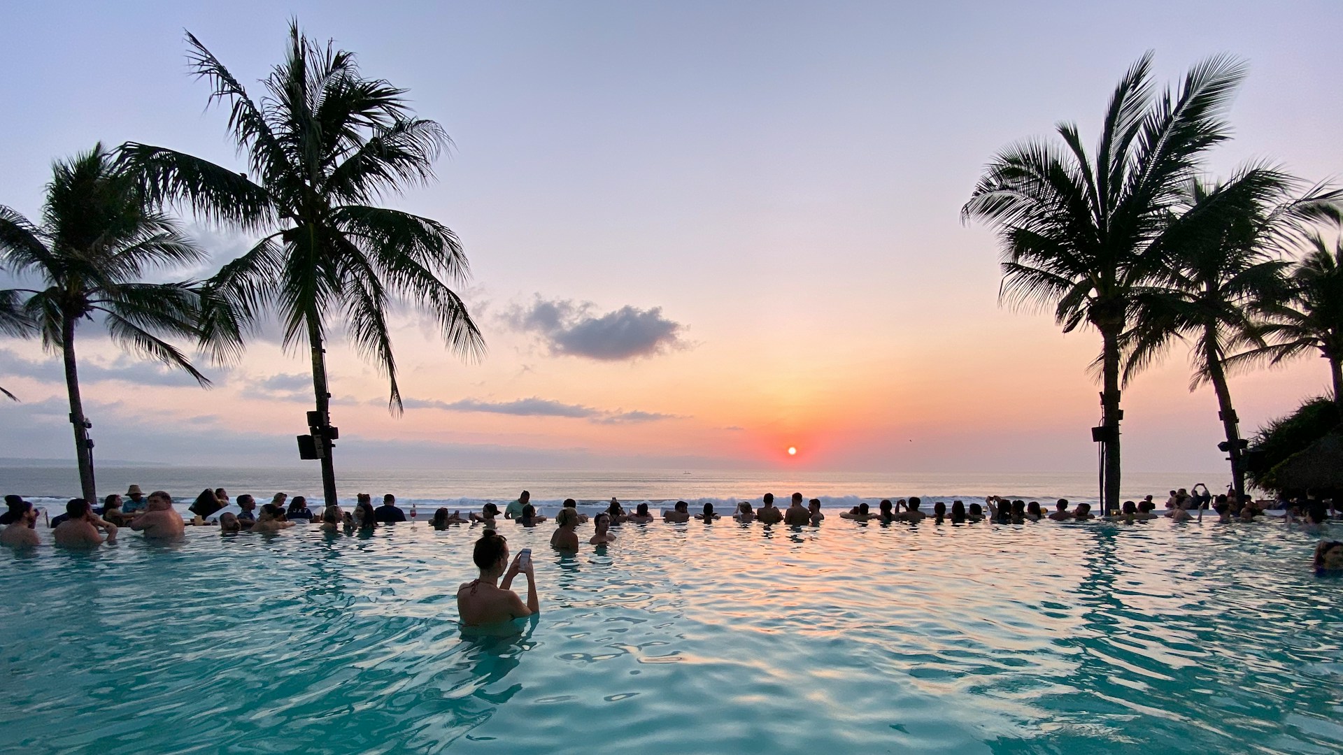 Bali beach resort infinity pool overlooking the ocean at sunset with palm trees Bali beach resort infinity pool overlooking the ocean at sunset with palm trees